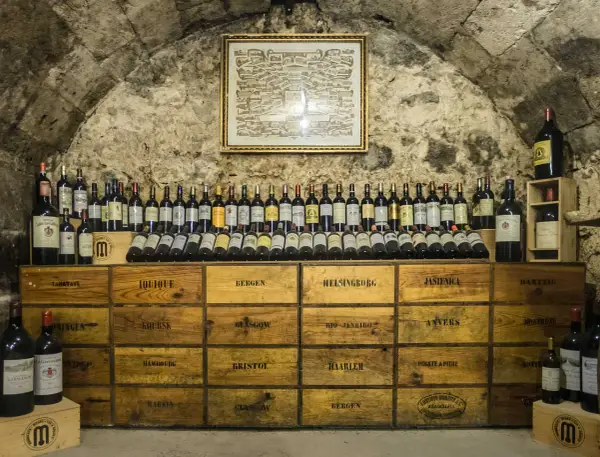 Cave voûtée avec une carte ancienne au mur, présentant une impressionnante liste des grands vins de Bourgogne, rangés sur des caisses en bois.