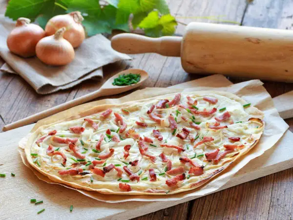 Flammekueche prête à être dégustée, avec ses oignons, lardons et ciboulette. Une recette facile pour un repas convivial.