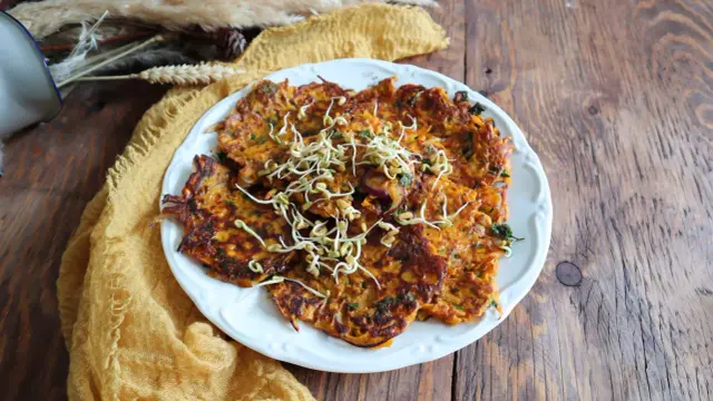 Galette de patate douce dorée, garnie de pousses fraîches, sur une assiette blanche, posée sur une table en bois rustique.