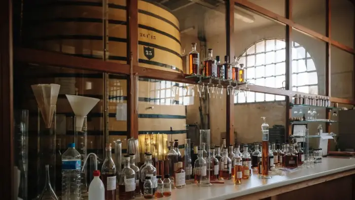 Dégustation de cognac français : flacons, éprouvettes et grands fûts en bois dans une cave de vieillissement.
