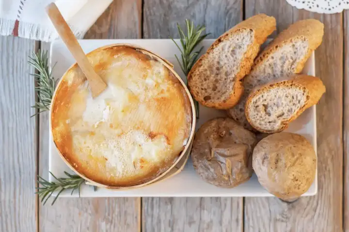 Un fromage à raclette fondant, une spécialité Jura, servi avec du pain croustillant et des pommes de terre.