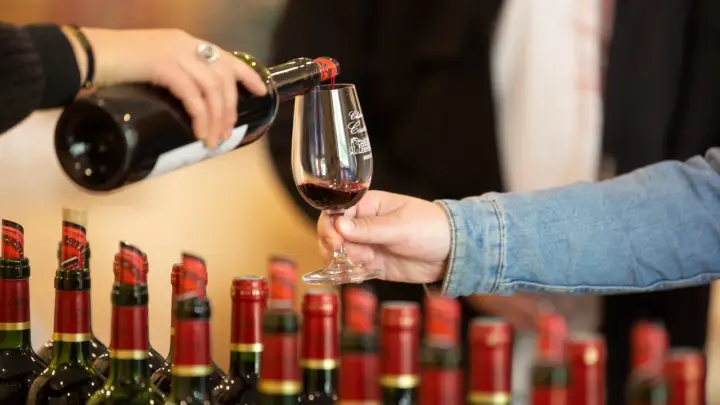 Dégustation de **vins de Bordeaux**, une main verse le liquide rubis dans un verre, tandis que d'autres bouteilles attendent leur tour.