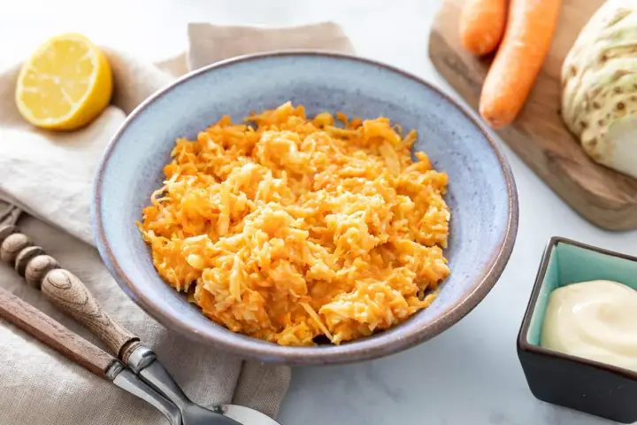Un bol de carottes râpées originales, avec un quartier de citron et une coupelle de mayonnaise à côté.