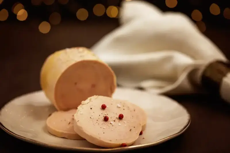 Tranche de foie gras, une des spécialités culinaires Dordogne, assaisonnée de poivre et de baies roses sur une assiette blanche.